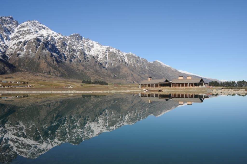Timber clubhouse reflected in a lake with mountains behind